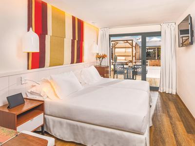 Bright hotel room with double bed and access to outdoor terrace with umbrella.