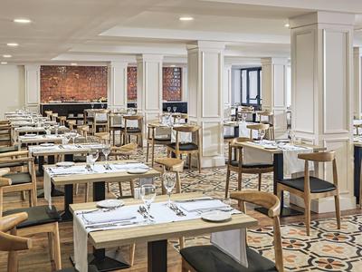 Spacious hotel dining area with wooden tables, chairs, white table settings, and elegant tiled floor.