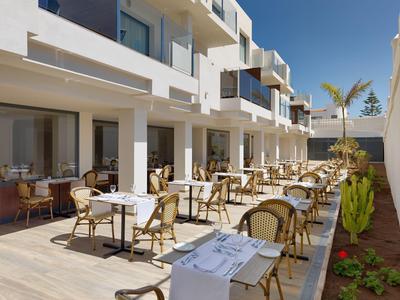 Outdoor dining area with tables and chairs by a modern hotel under clear blue sky.