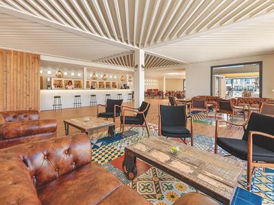 Stylish lounge area with patterned floor tiles, leather chairs, and a white bar in the background.