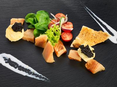 Elegant dish with smoked salmon, greens, crackers topped with black caviar on slate plate.