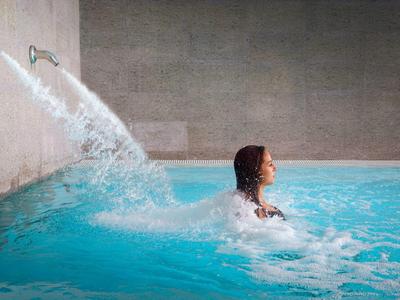 Person relaxing in an indoor pool with water flowing from two pipes into the water.