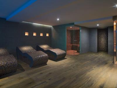 Modern spa room with dark cushioned lounge chairs and a wooden sauna on the right.