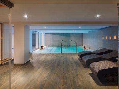 Indoor pool area with lounge chairs and hardwood floors under soft lighting.