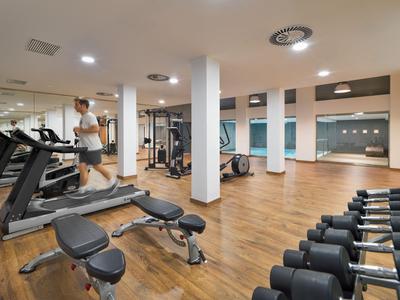 Moderner Fitnessraum mit Laufbändern, Hanteln und Geräten auf Holzboden.