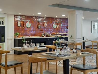 Modern hotel restaurant with wooden tables and black chairs against a red brick wall design.
