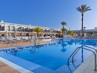 Hotel pool with blue water surface, surrounded by lounge chairs and palm trees under a clear sky.