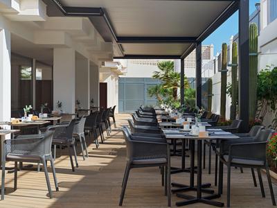 Modern open-air restaurant with tables and chairs under a covered area.
