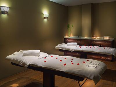 A tranquil spa room with two massage tables, brown walls, and soft lighting.