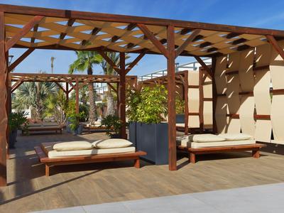 Modern outdoor area with wooden garden furniture, plants, and pergola under clear blue sky.
