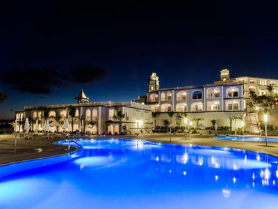 Hotel illuminato con grande piscina all'aperto di notte sotto un cielo limpido.