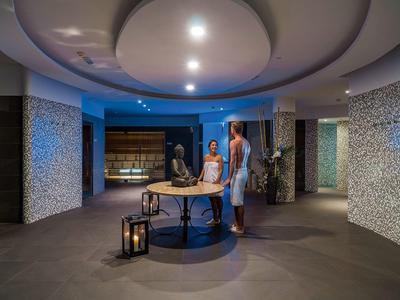 Moderna hall dell'hotel con soffitto rotondo, sculture in pietra e due persone al tavolo centrale.