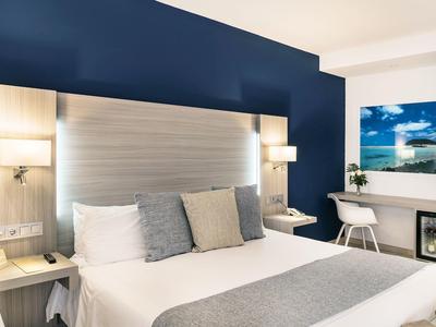 Camera d'hotel moderna con grande letto, testiera grigia e scrivania vicino alla finestra.