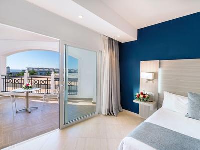 Camera d'hotel luminosa con parete blu, letto, balcone e vista mare.