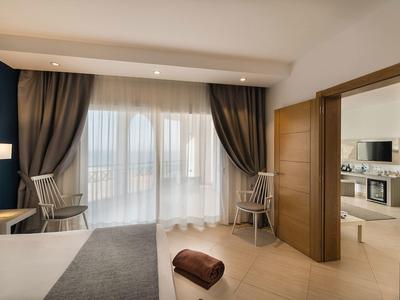 Camera d'hotel moderna con letto, due sedie davanti a grandi finestre e vista su una cucina.