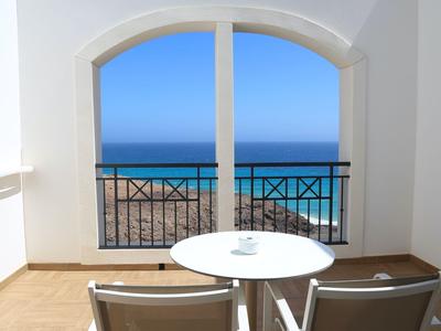 Balcone con tavolo e sedie che si affaccia sul mare azzurro sotto un cielo limpido.