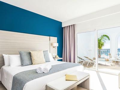 Camera d'hotel luminosa con grande letto, accenti grigi e balcone con vista sul mare.