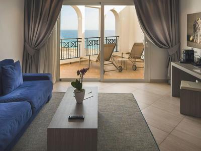 Camera moderna con divano blu, scrivania e balcone con vista sul mare.