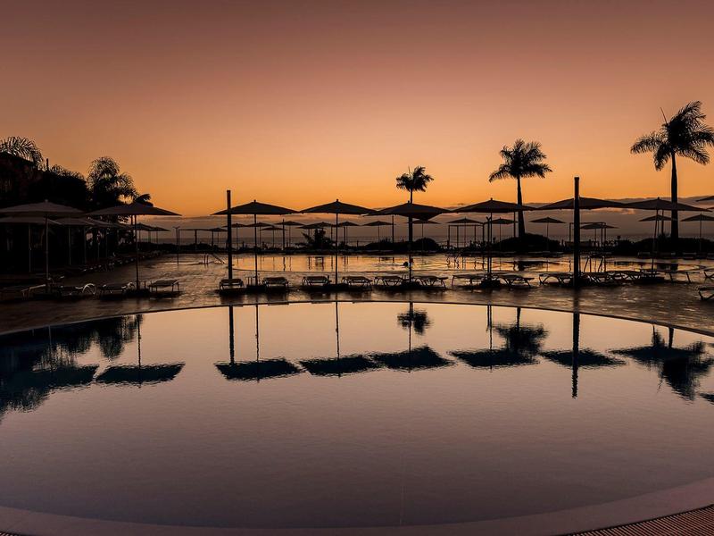 Tramonto su una piscina con ombrelloni e palme, atmosfera tranquilla.