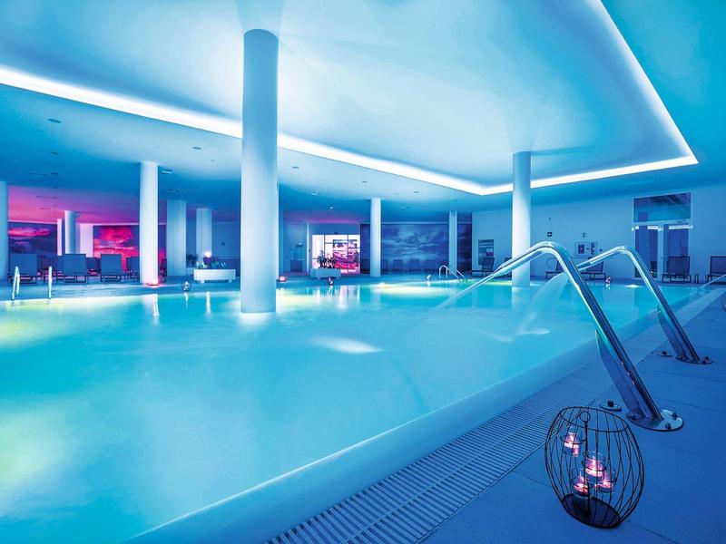 Piscina interna moderna illuminata con giochi d'acqua e luce di candela in un'atmosfera tranquilla.