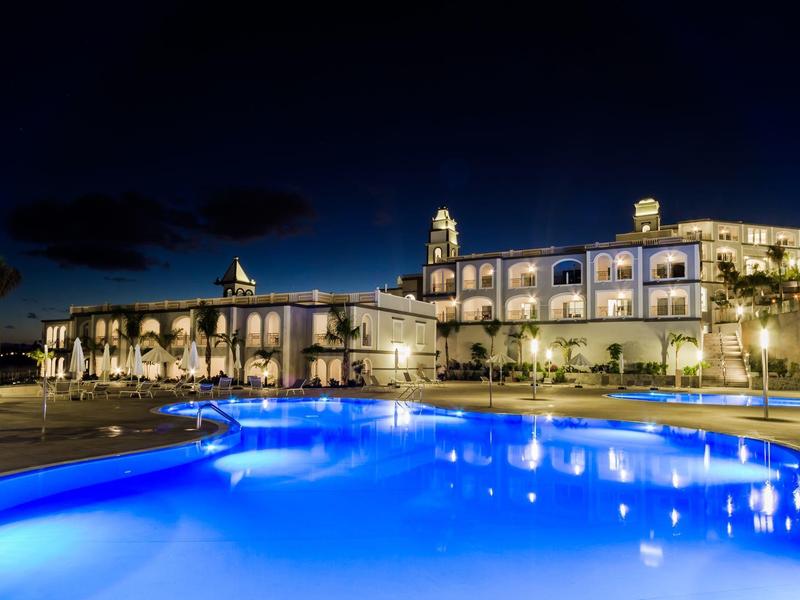 Hotel illuminato con grande piscina all'aperto di notte sotto un cielo limpido.