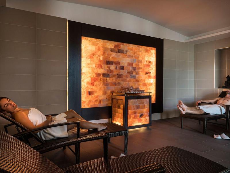 Sauna moderna con lettini relax e parete illuminata in mattoni di sale.