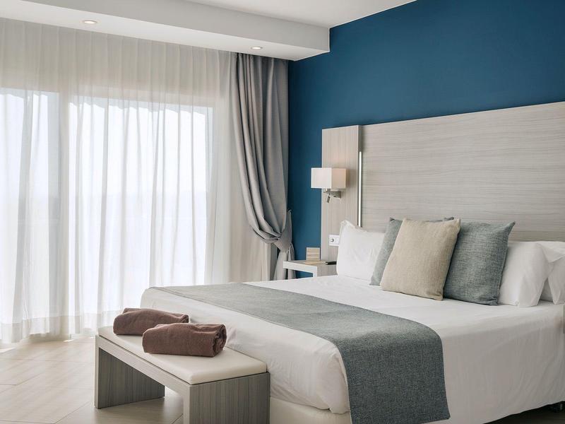 Camera d'hotel moderna con letto matrimoniale, panca e grandi finestre con tende.