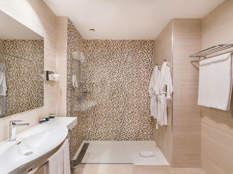 Bagno luminoso con doppi lavandini e doccia a pioggia con parete a mosaico.