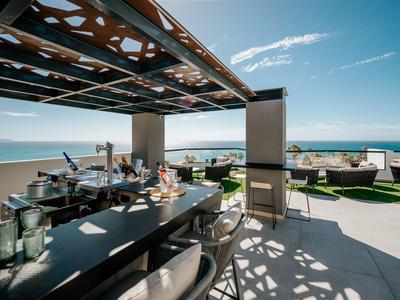 Moderner Außenbereich mit Bar, Sitzplätzen und Blick auf das blaue Meer unter klarem Himmel.