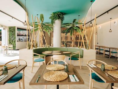 Modernes, helles Restaurant mit grünen Sitzplätzen, Bambuspflanzen und Holztischen, sanfte Beleuchtung.