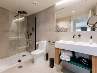 Moderner Badezimmerspiegel, weiße Toilette, Duschecke mit Glaswand, weißes Waschbecken, graue Fliesen.
