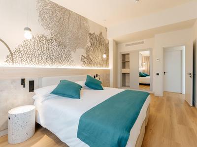 Modernes Schlafzimmer mit Doppelbett, türkisfarbenen Akzenten, hellem Holzboden und abstrakter Wandgestaltung.