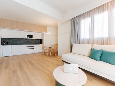Helles Wohnzimmer mit weißer Küche, Holzboden, Sofa mit blauen Kissen und kleinem runden Tisch.