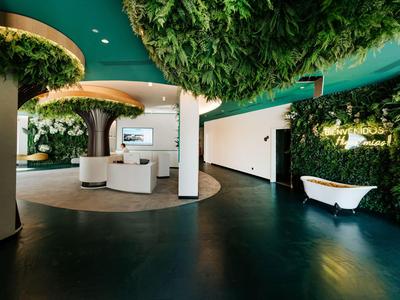 Nowoczesna lobby hotelowa z zielonymi roślinami na ścianach, okrągłymi miejscami do siedzenia i wolnostojącą wanną.