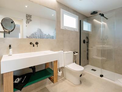 Modernes Badezimmer mit weißem Waschbecken, Toilette, großer Glasdusche und hellem Fliesendesign.