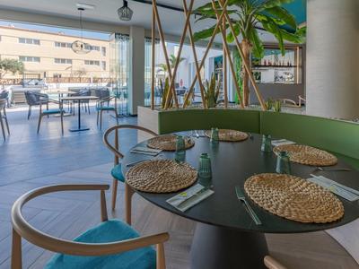 Modernes Restaurant mit runden Tischen, grünen Stühlen und großen Glasfenstern zum Außenbereich.