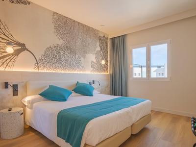 Modernes Schlafzimmer mit Doppelbett, blauen Kissen und Decken, Holzfußboden und Wandkunst.