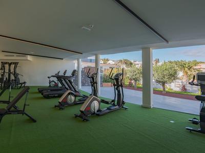 Ein moderner Fitnessraum mit Sportgeräten auf grünem Kunstrasen und Blick auf Außenpool.