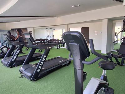 Moderne Fitnessraum mit Laufbändern, Fahrrädern und multifunktionalen Trainingsgeräten auf grünem Boden.