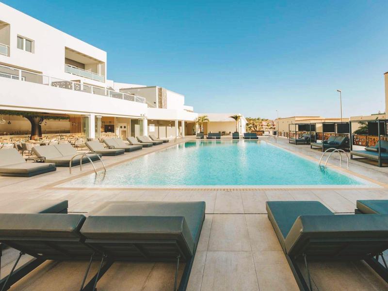 Piscina esterna moderna con lettini in un elegante hotel al tramonto.