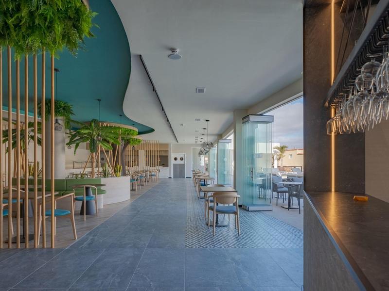 Area ristorante di un hotel moderno con molta luce naturale, piante e design contemporaneo.