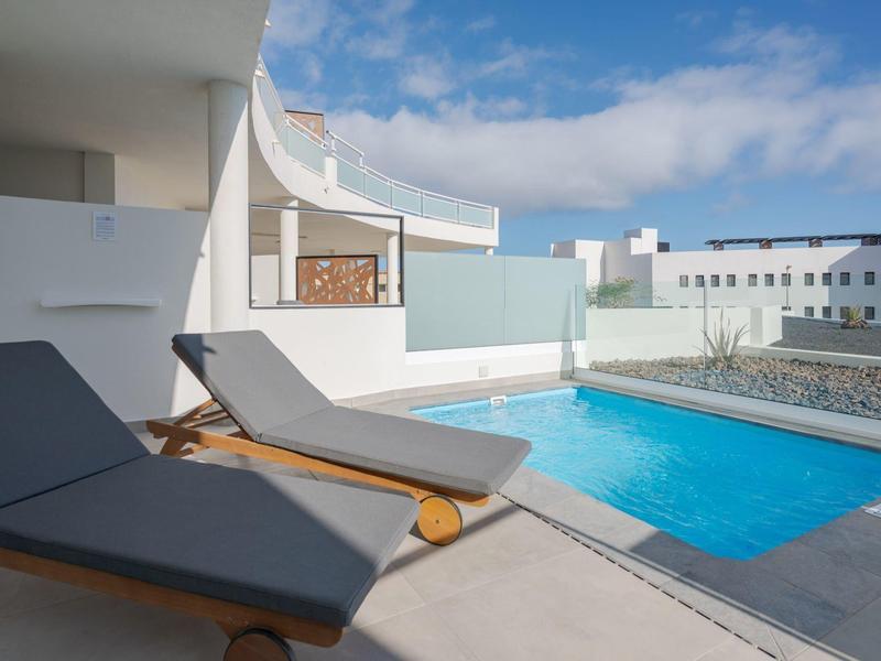 Area esterna moderna con piscina e due lettini prendisole in una giornata soleggiata.