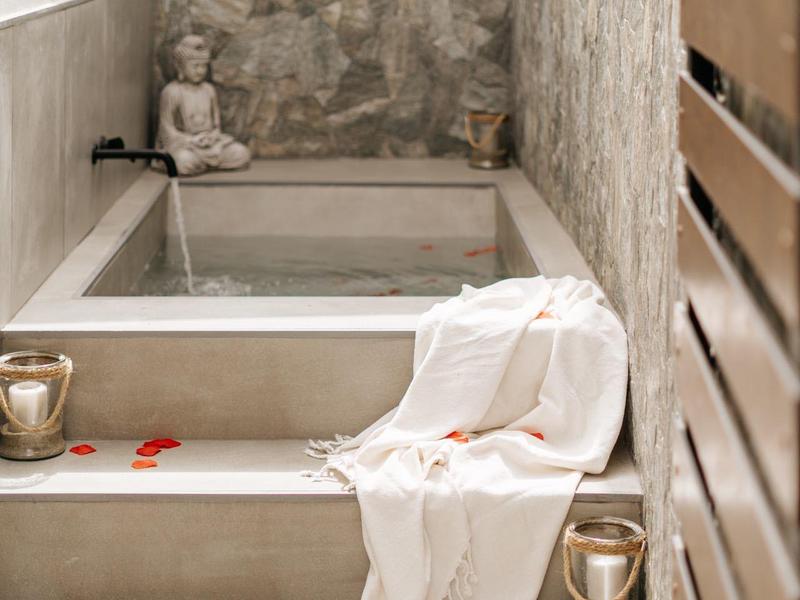 Area benessere accogliente con vasca idromassaggio, asciugamani bianchi, candele e petali di rosa.