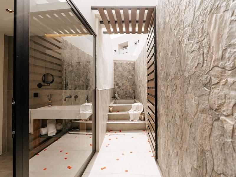 Area bagno di un hotel moderno e luminosa con pareti in pietra, scale e parete divisoria in vetro.