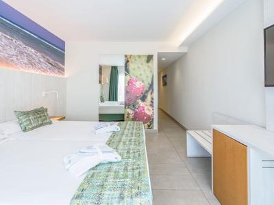 Camera d'hotel moderna con letto matrimoniale, cuscini verdi a motivi e grande quadro murale della spiaggia.