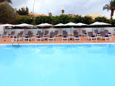 Großer Swimmingpool mit blauer Wasserfläche, umgeben von Liegestühlen und weißen Sonnenschirmen.