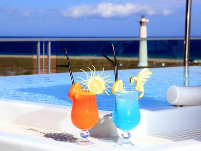 Zwei bunte Cocktails mit Sonnendekoration am Pool mit Leuchtturm im Hintergrund.