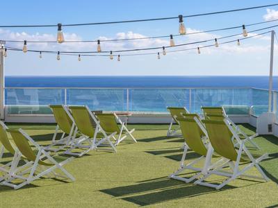 Terrazza sul tetto con sedie a sdraio con vista sul mare sotto un cielo azzurro.