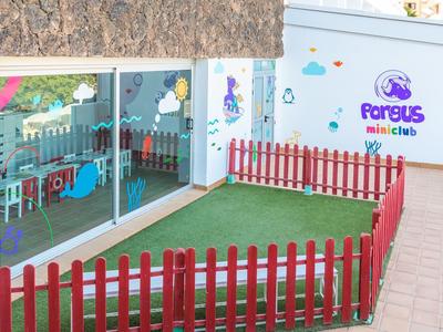 Piccola area esterna con prato sintetico verde e recinzione rossa davanti a stanze con finestre