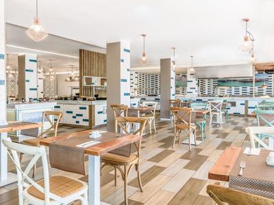 Sala da pranzo luminosa e moderna con tavoli e sedie in legno in un hotel.